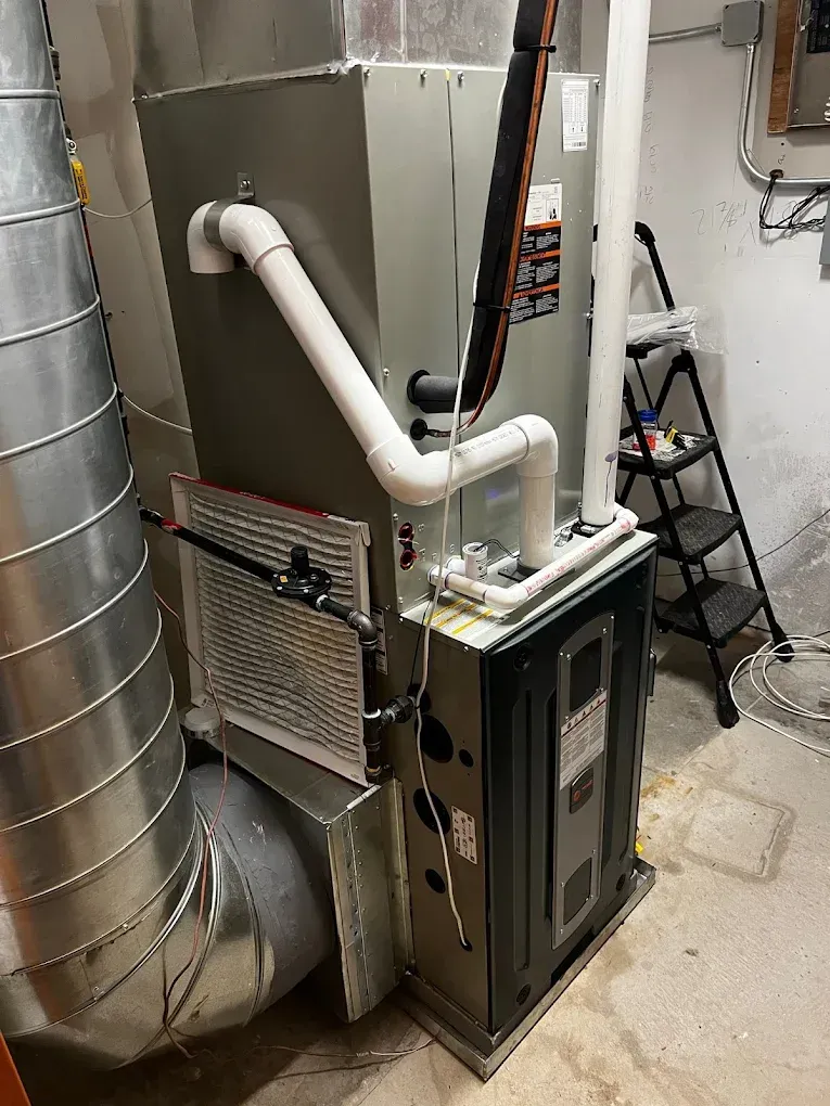 HVAC furnace and ductwork in a utility room with white pipes and a metal vent hose