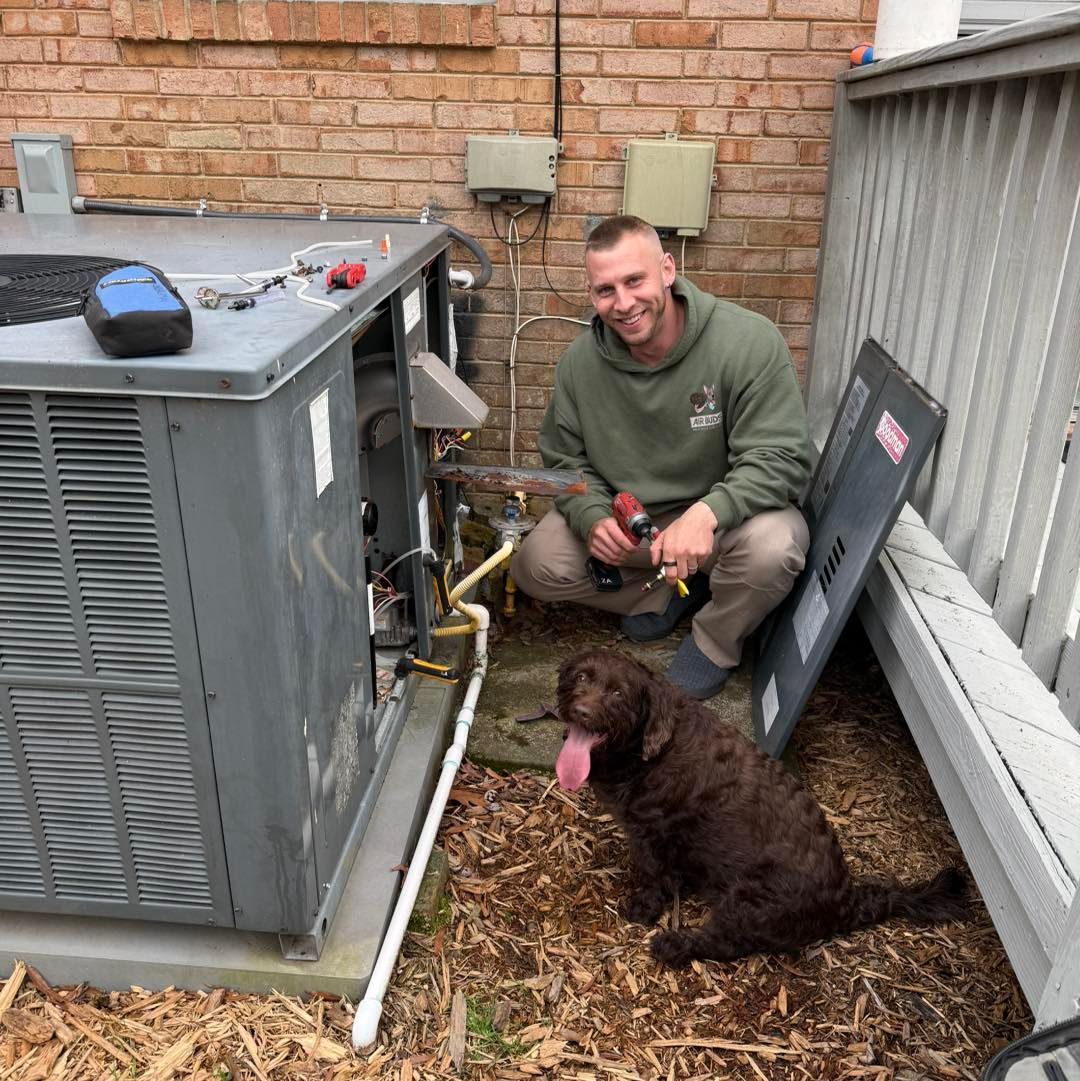 Technician kneeling beside HVAC unit outdoors with a brown dog nearby, tools in hand.