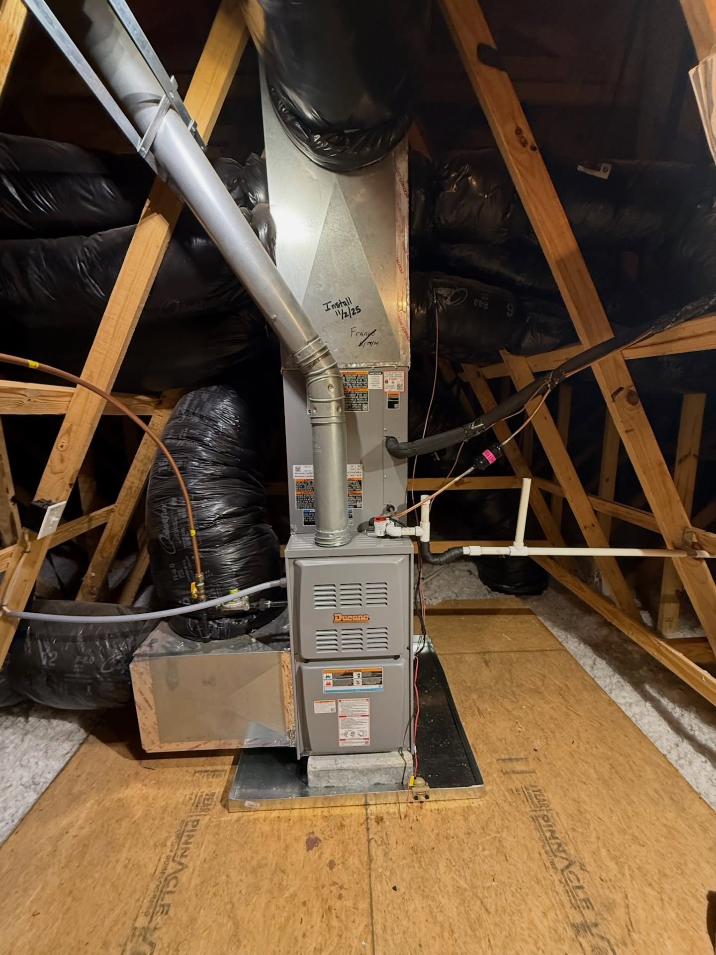 Attic HVAC furnace and ductwork amid exposed wooden rafters and insulation
