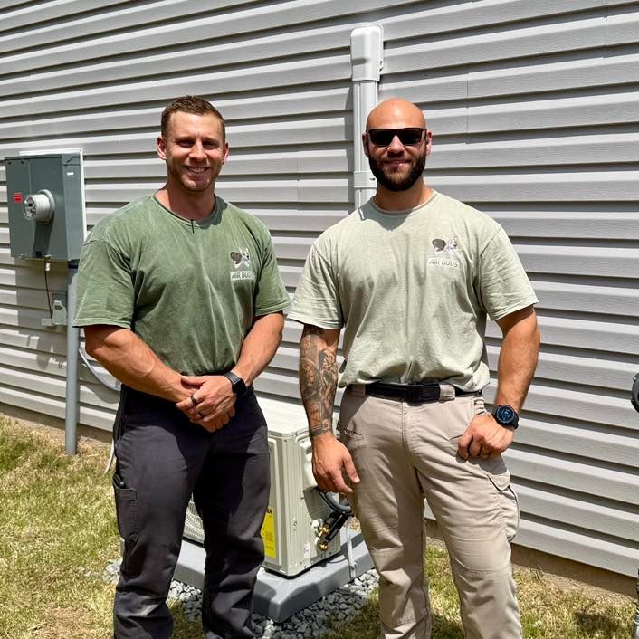 Two men standing beside an outdoor electrical unit against a corrugated metal wall.