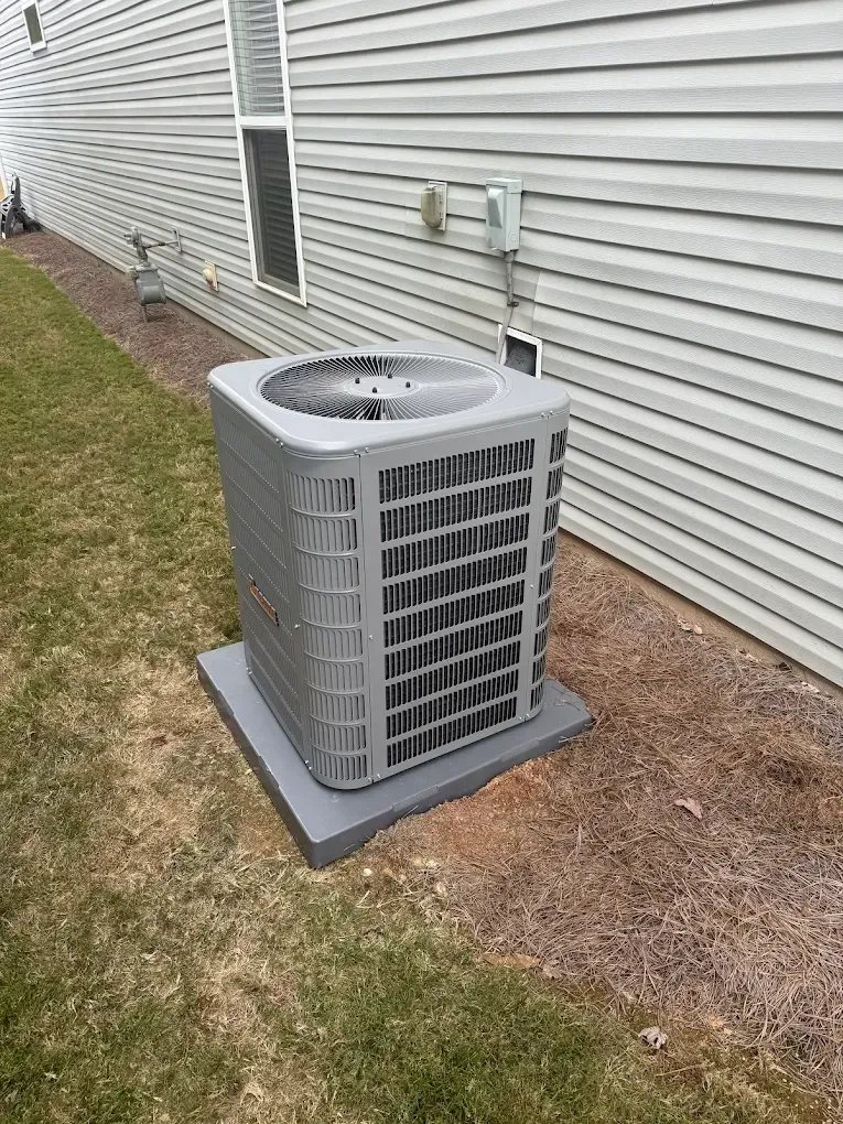 Outdoor air conditioner unit beside a house with white siding and a grassy yard