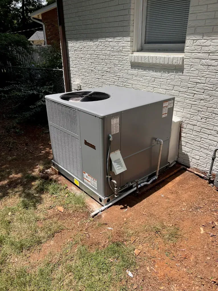 Outdoor air conditioner unit beside a house on a brick-and-grass yard.