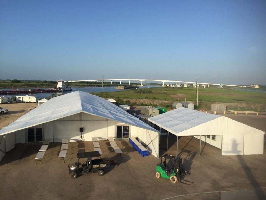 White tents on a paved area near a river, with a bridge in the background, and a golf cart and forklift in the foreground.