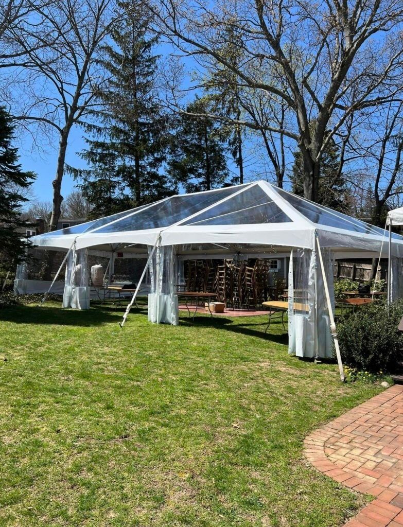 A clear tent set up on green grass with trees in the background.