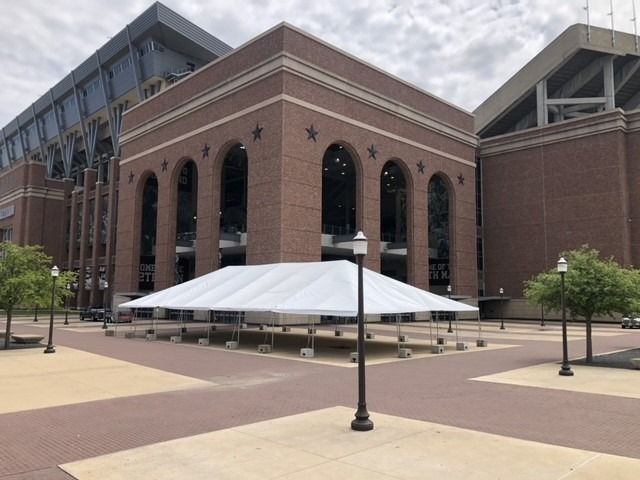 Exterior view of a brick building with large arched windows, a white tent in front, and a paved plaza.