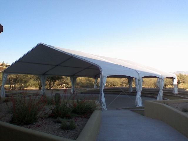 White tent set up outdoors, casting shade over a paved area, sunny day.