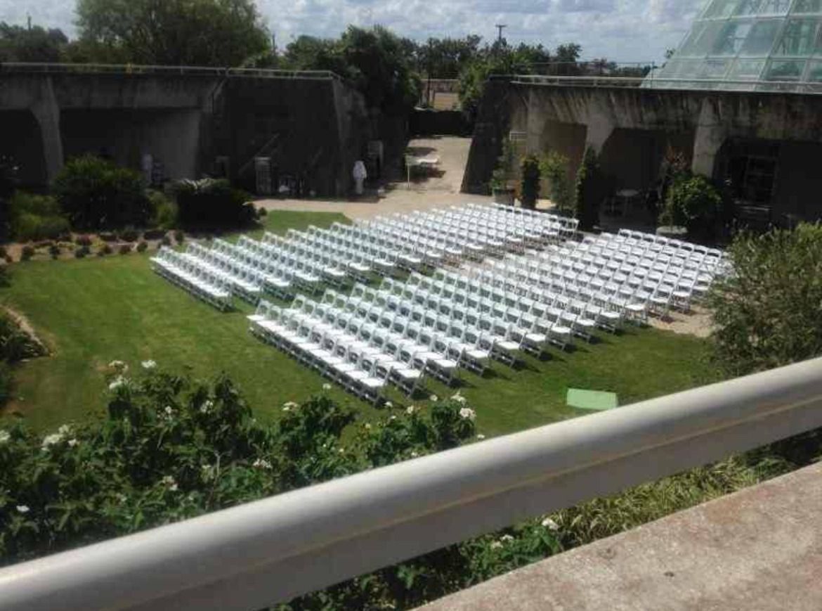 Rows of white chairs set up on a grassy area, likely for an outdoor event, near concrete structures and greenery.