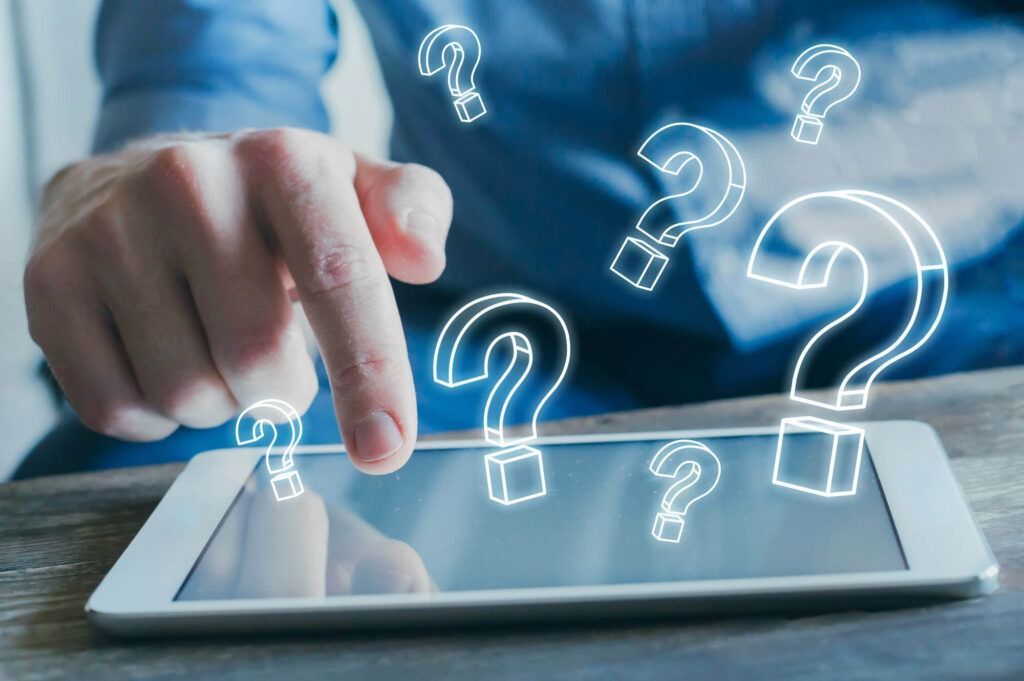 Person's hand touching tablet screen with glowing question mark symbols over it.
