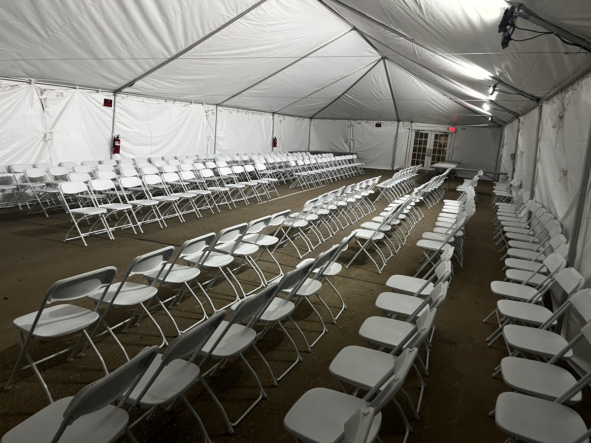 Rows of white folding chairs set up inside a large white tent.