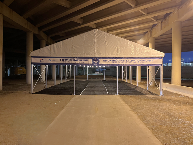 Tent under a concrete overpass, with a sign for a project, likely for a construction site.