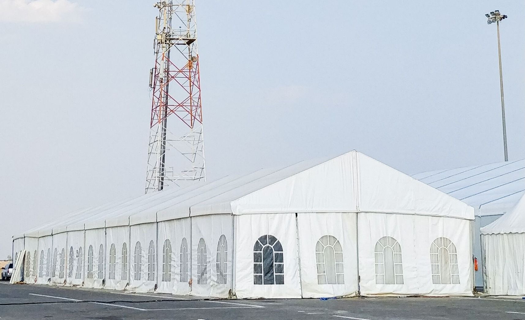 White tents in a row, possibly for a large event, with a communication tower in the background.