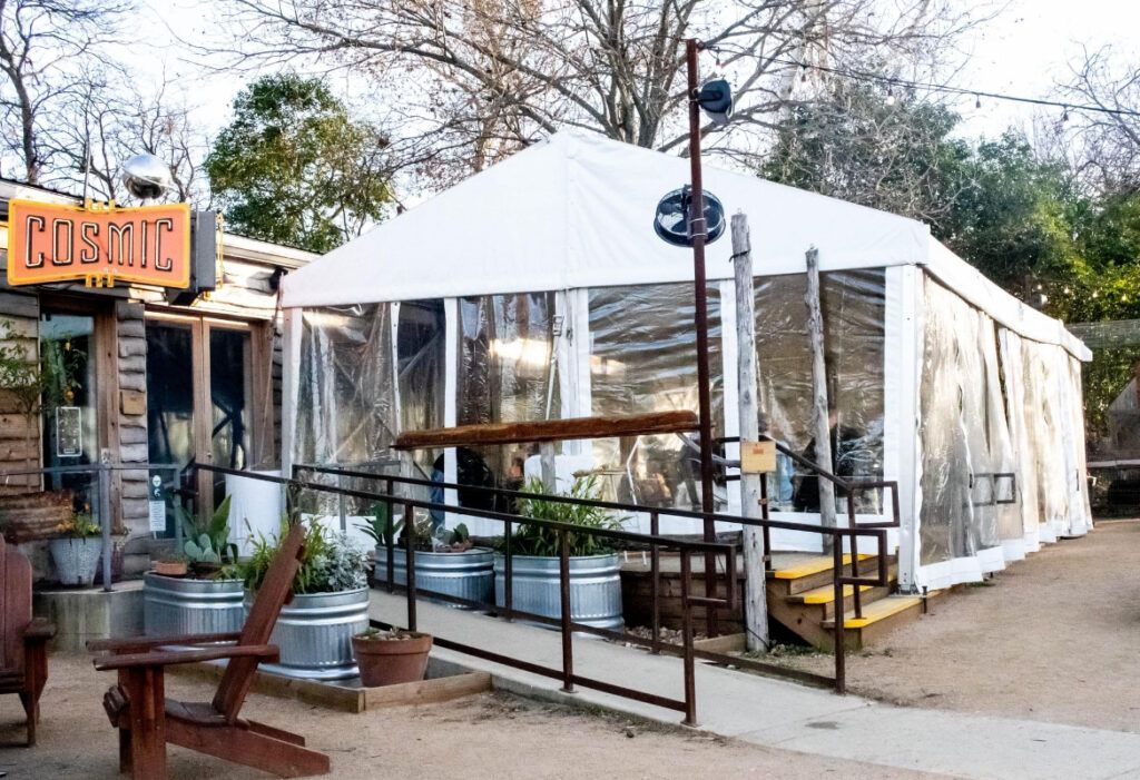 Outdoor restaurant with a white tent enclosure. Includes a wheelchair ramp and wooden building with signage.