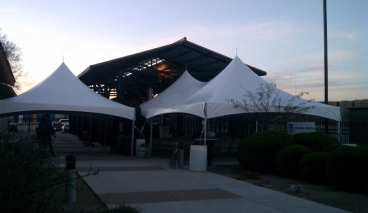 White tents set up on a sidewalk in front of a building, evening light.