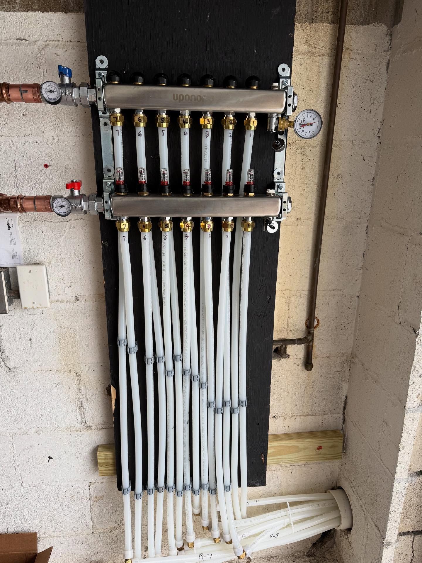 Residential plumbing manifold with multiple labeled white pipes and gauges on a wall.
