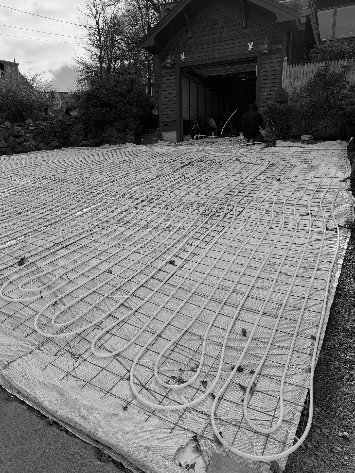Radiant floor heating tubes laid over concrete mesh in a driveway beside a house entrance