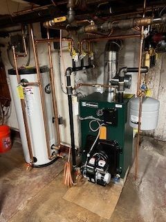 Basement utility room with boiler, water heater, pipes, and plumbing equipment.