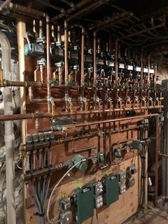 Industrial room with dense copper pipes, valves, and gauges along a wall