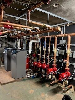 Basement mechanical room with pipes, valves, pumps, and HVAC equipment in red, copper, and gray.