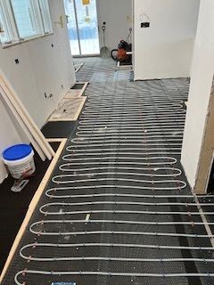Curved white radiant floor heating tubes installed over black underlayment in a hallway under renovation