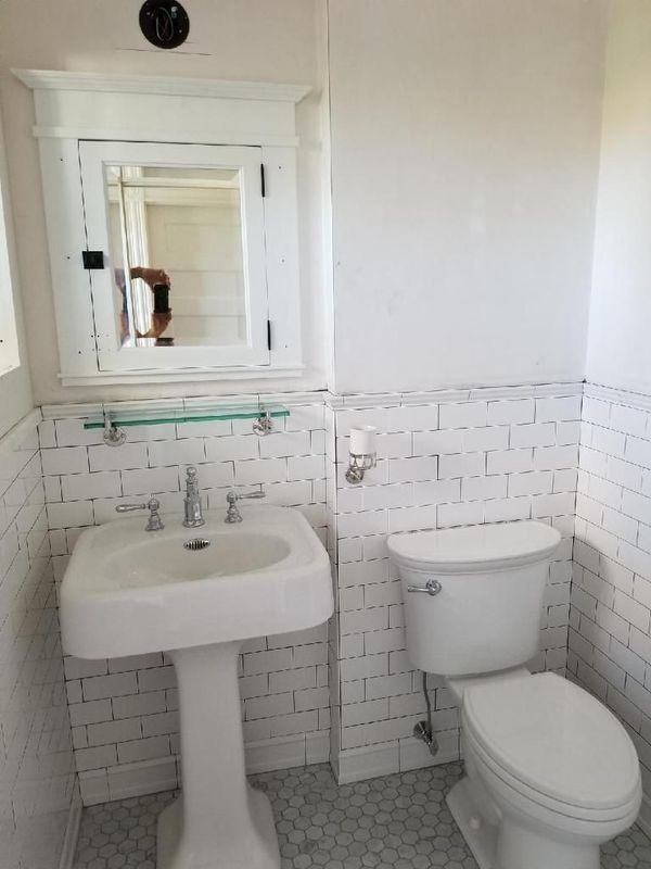 Small white bathroom with pedestal sink, mirror cabinet, toilet, and white tiled walls.