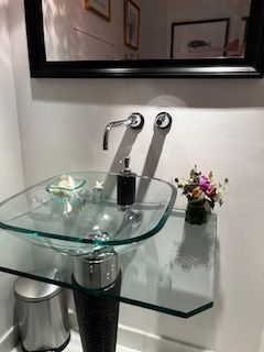 Modern glass bathroom sink with chrome faucet, soap dish, towel ring, and small flower arrangement