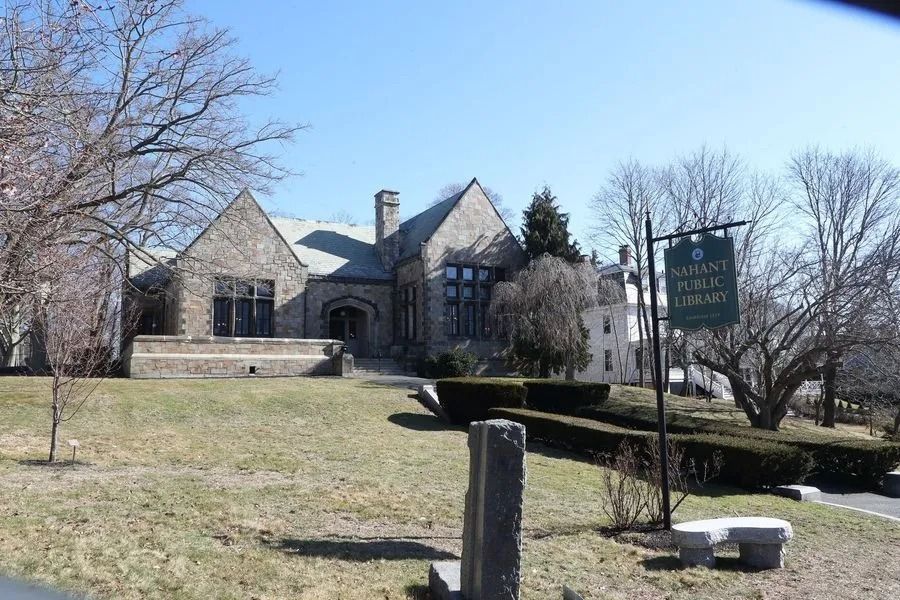 Stone house on a grassy hill with leafless trees and a green sign in front.
