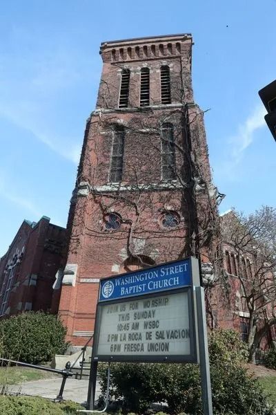 Historic brick church tower with blue sign and white marquee under a clear sky