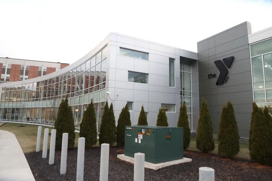 Exterior of a modern YMCA building with glass windows, trees, and white bollards in front