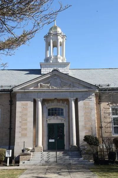 Historic stone building with a columned entrance and white cupola under a clear blue sky