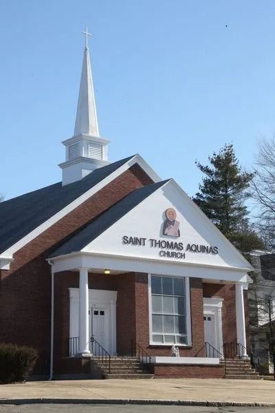 Saint Thomas Aquinas Church with white steeple and brick facade under a clear blue sky