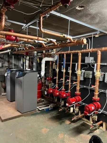 Industrial boiler room with red pumps, copper piping, and gray equipment in a mechanical basement
