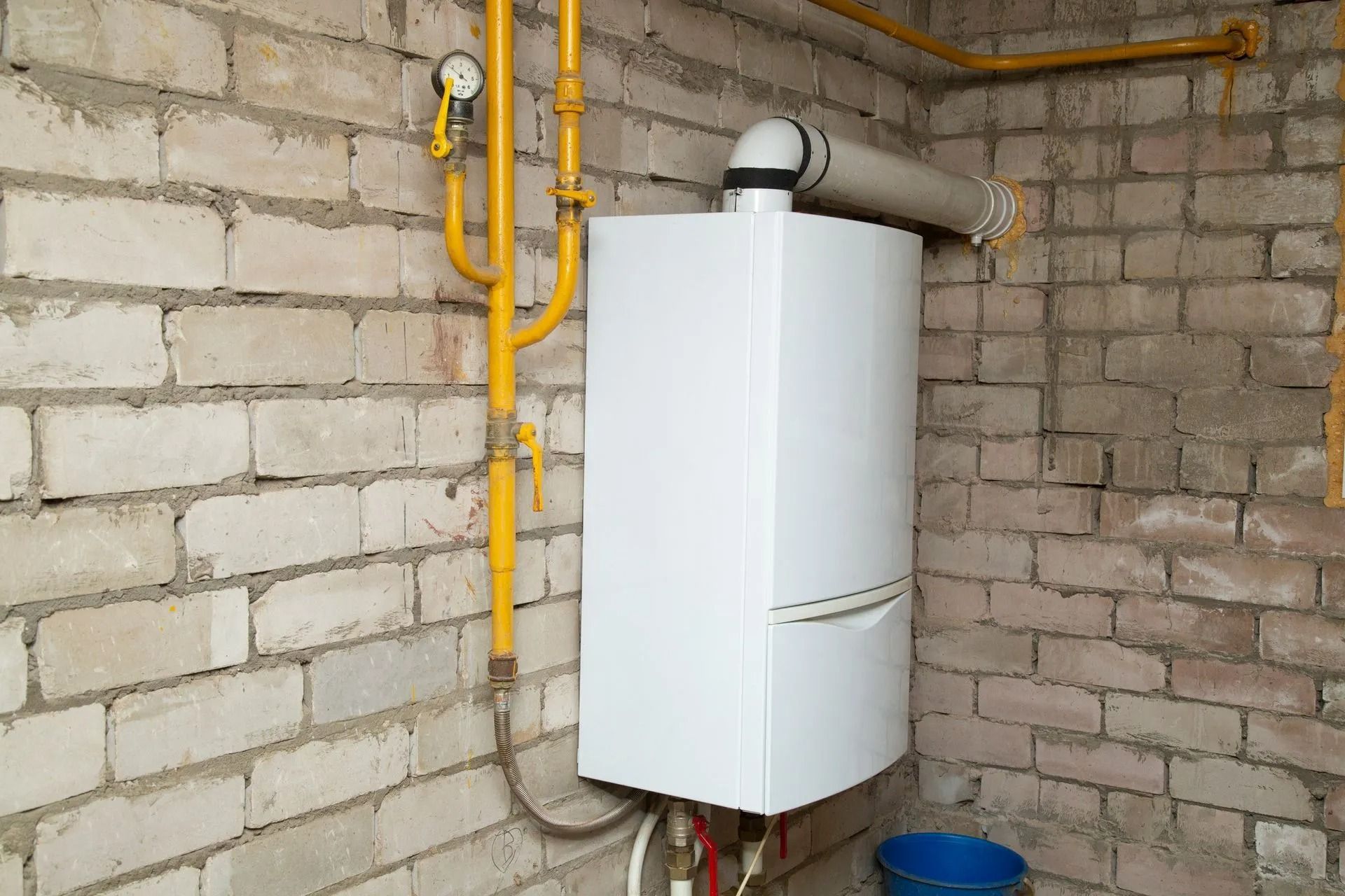 Wall-mounted white boiler with yellow gas pipes in a bare cinder block utility room
