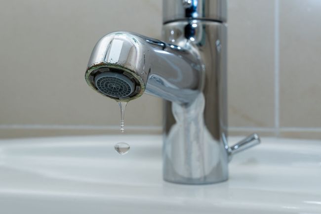 Close-up of a chrome bathroom faucet dripping water into a white sink