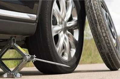 Picture of a Vancouver Tow Truck car jack under a black car with a spare tired leaned up against the bumper.