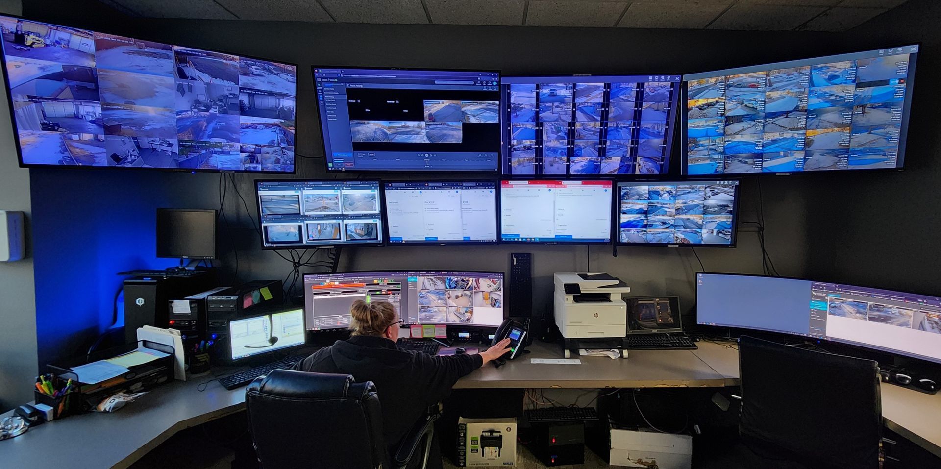 A man is sitting at a desk in front of a wall of monitors.