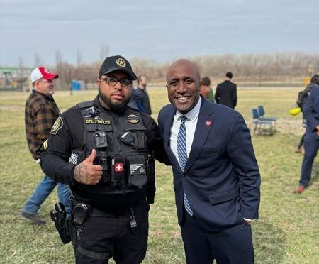 A police officer and a man in a suit are posing for a picture in a field.