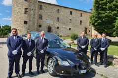 Un gruppo di uomini in giacca e cravatta sono in piedi davanti a un carro funebre nero.