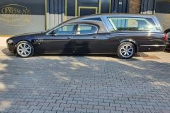 Un carro funebre nero è parcheggiato su un vialetto in mattoni di fronte a un edificio.