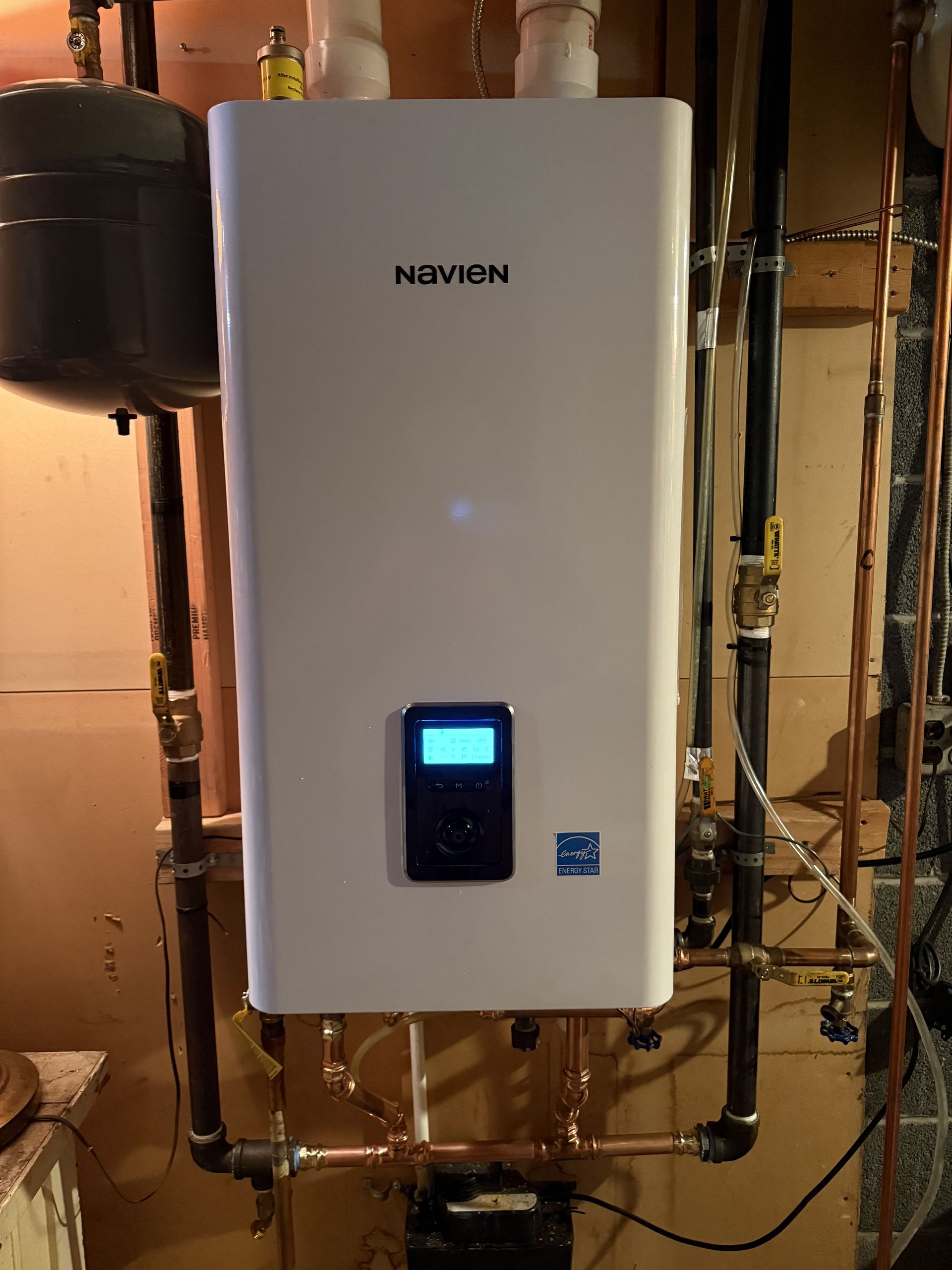 Wall-mounted white boiler with blue-lit display and copper pipes in a utility room
