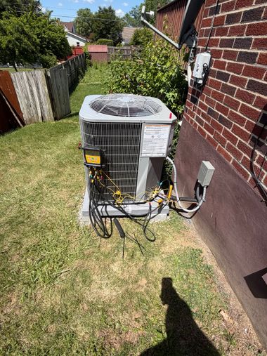 Outdoor air conditioner unit beside a brick house in a narrow grassy side yard.