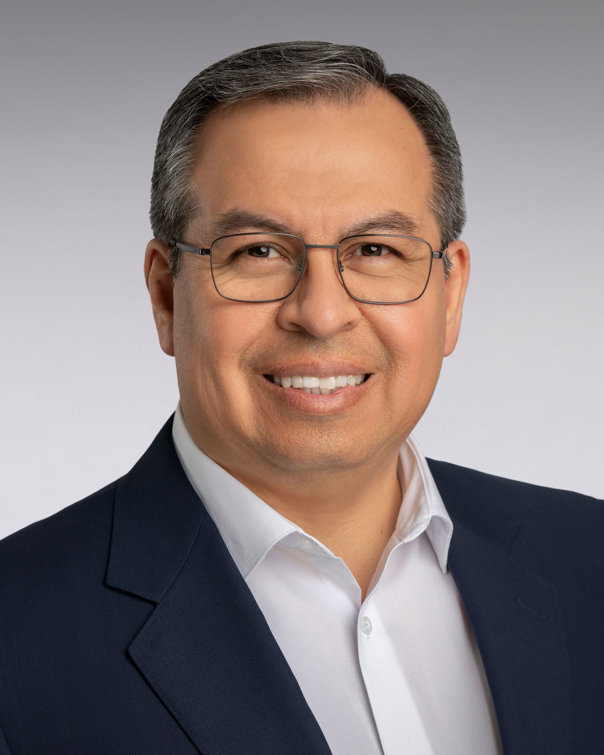 Professional headshot of a smiling person in a navy blazer and white shirt against a gray background