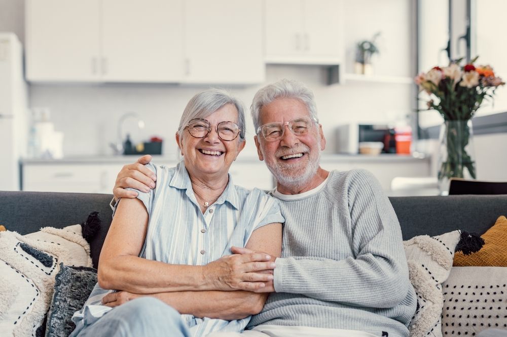 Elderly couple smiling and embracing on a sofa.