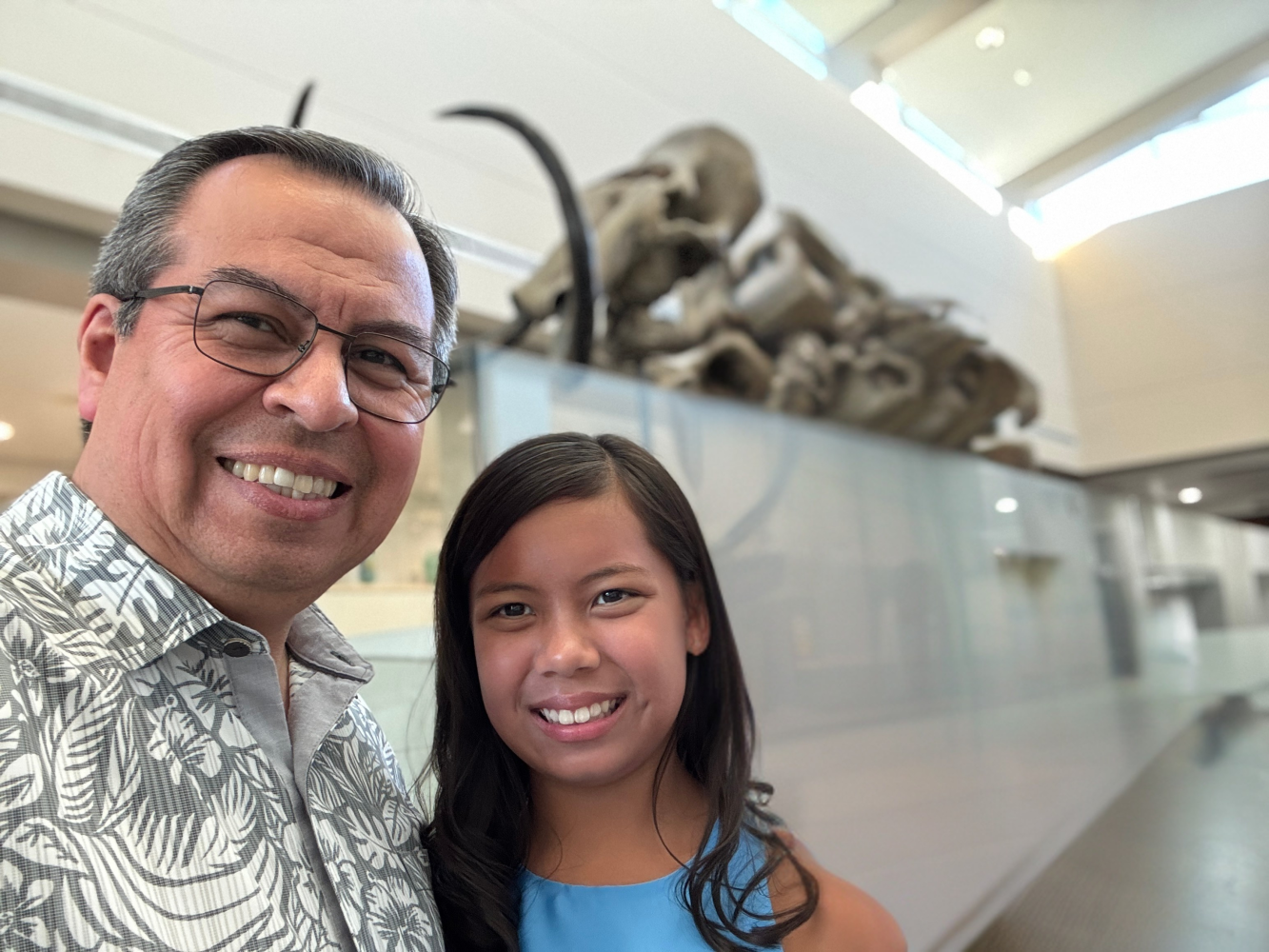 Two people smiling for a selfie in a bright indoor museum exhibit