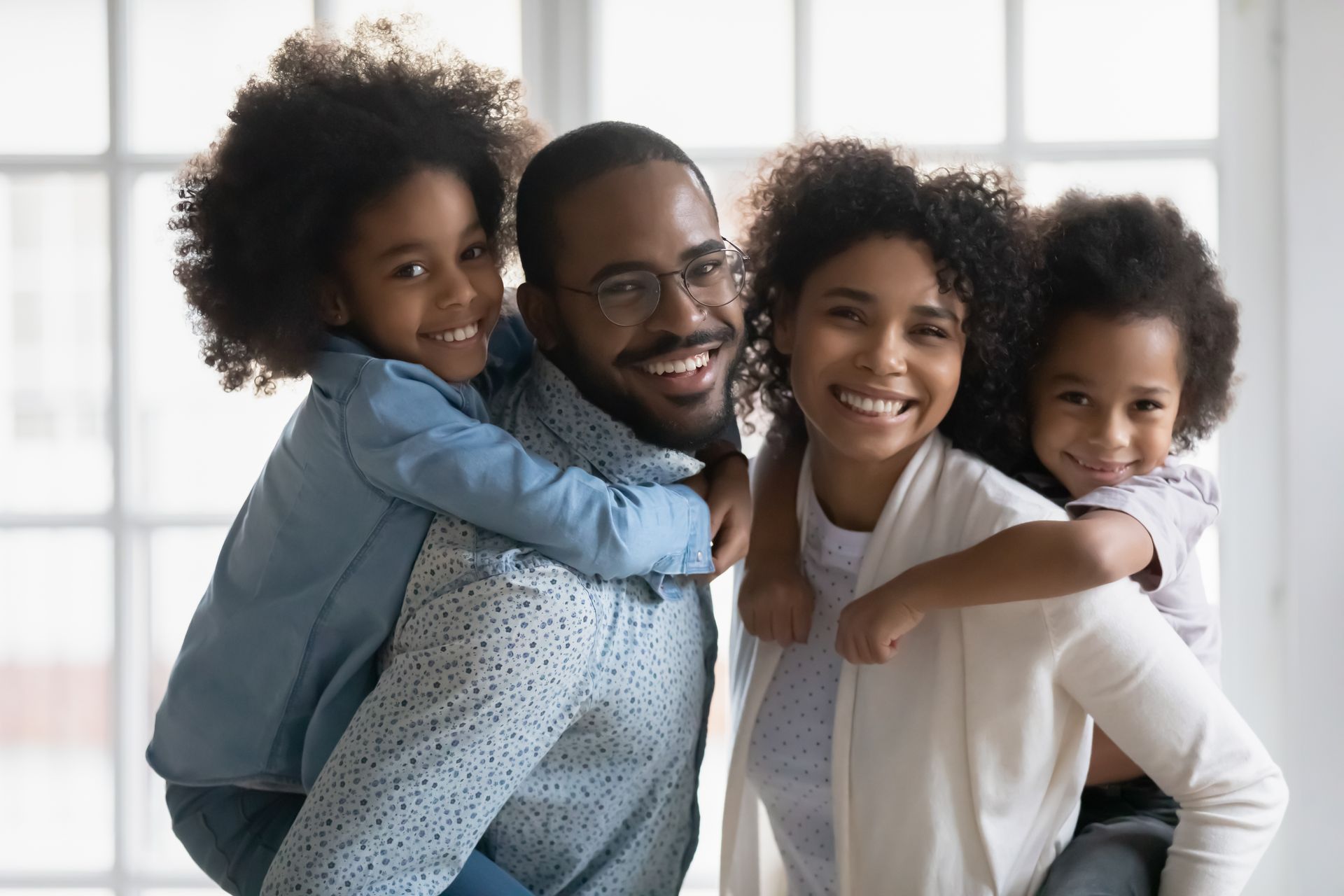 Four smiling people posing together in a bright indoor setting, with two children hugging the adults.