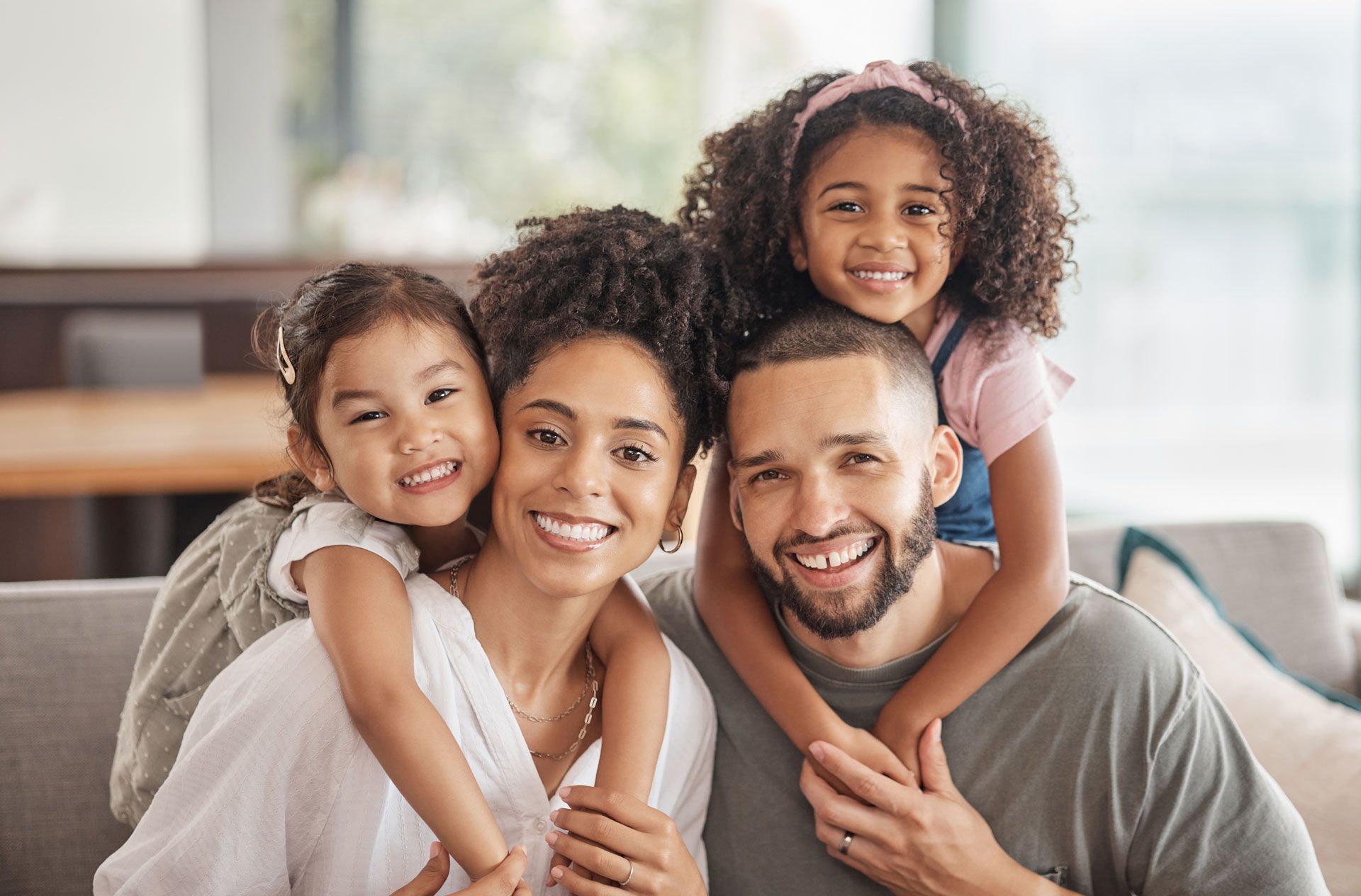 Smiling family of four cuddling on a couch in a bright living room