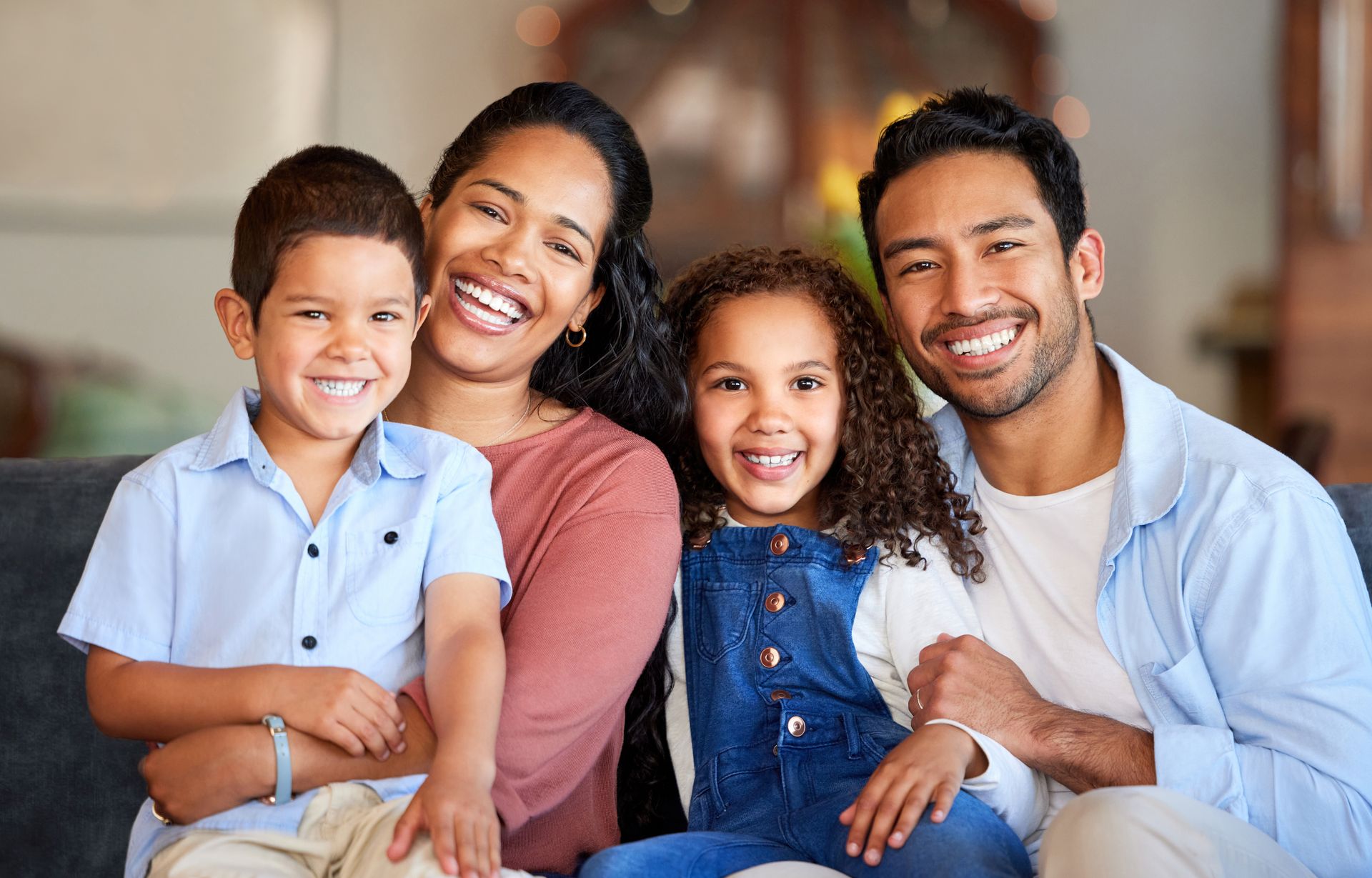Smiling family of four seated together indoors, with two adults and two children in casual clothes.
