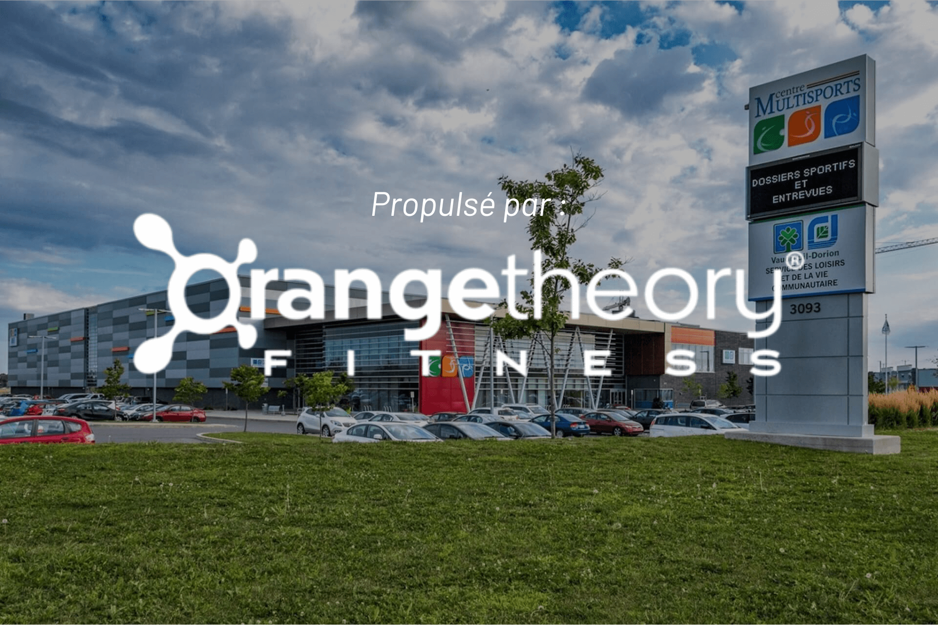 Logo d'Orangetheory Fitness devant un centre commercial par une journée ensoleillée.