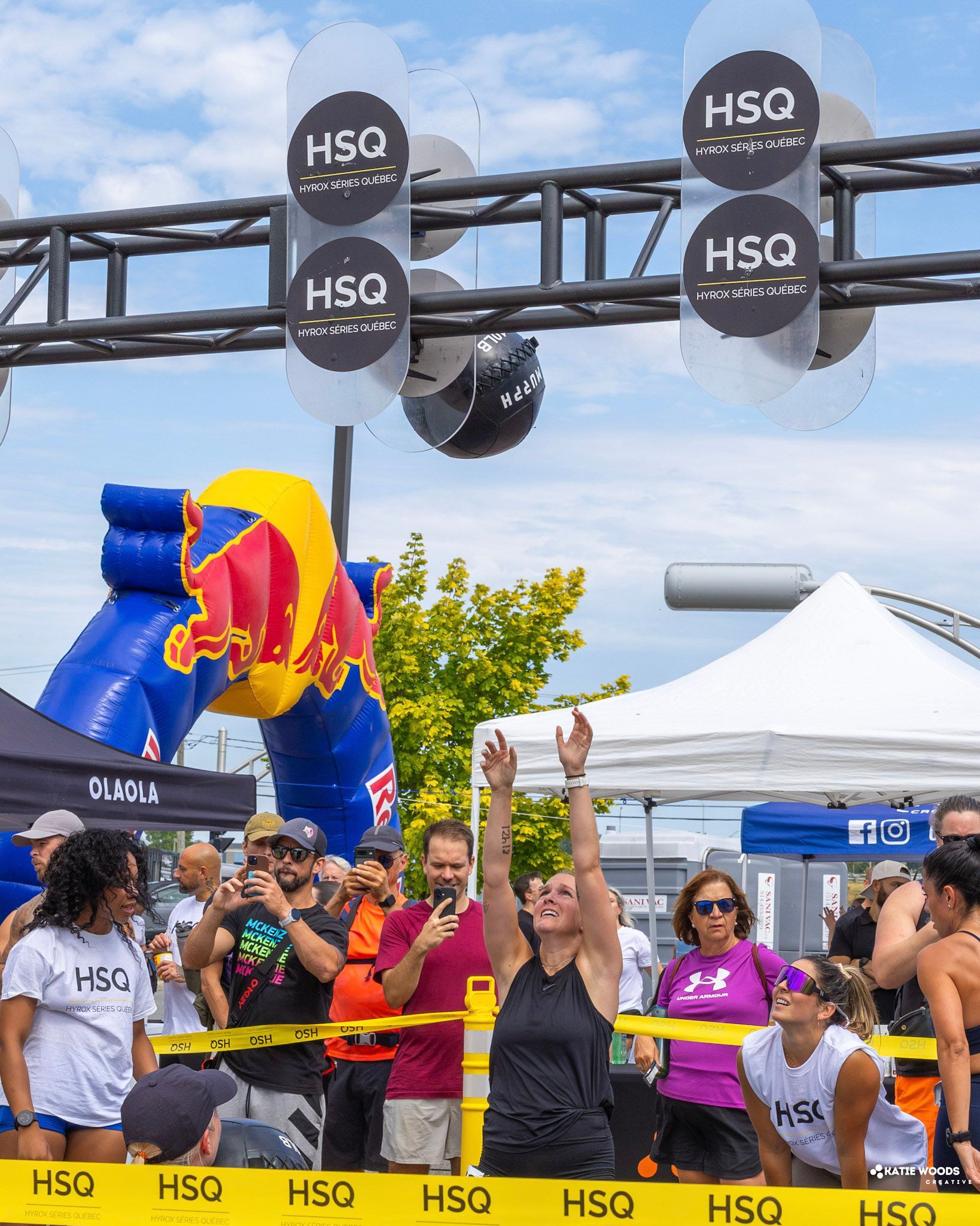 Crowd cheering under HSQ arch at outdoor festival with colorful inflatable and tents in the background