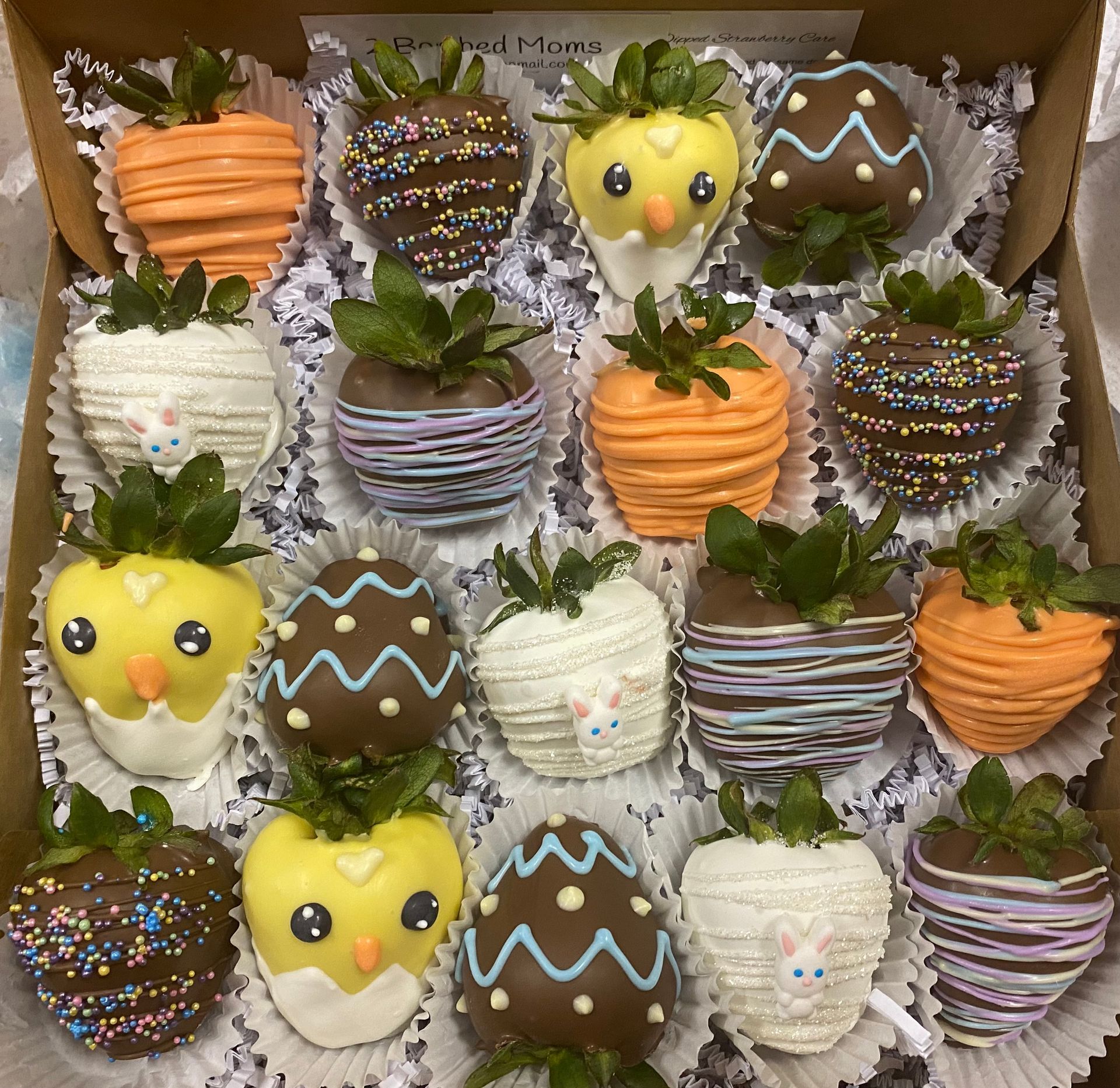 Assorted chocolate-covered strawberries in a box, decorated with sprinkles, stripes, and cute faces