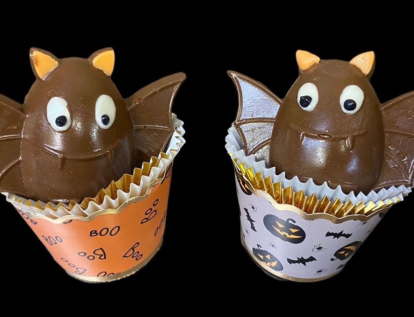 Two chocolate cat-shaped desserts in orange and white wrappers on a black background